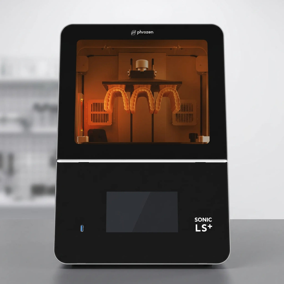 Phrozen Sonic LS+ dental resin 3D printer, front view, with an amber lit chamber showing a printed dental arch model attached to the build plate.